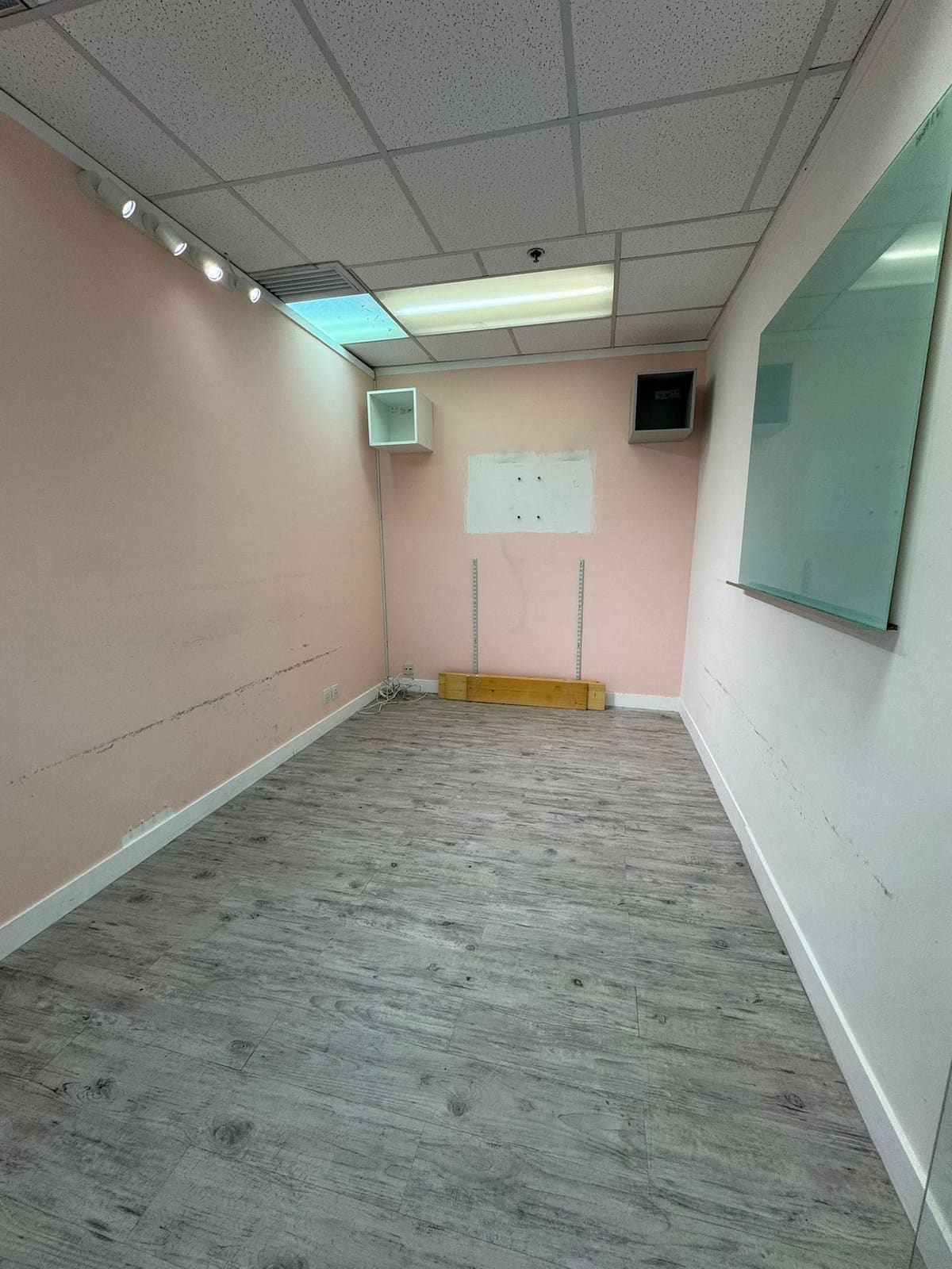 Empty room on Leighton Road with pink walls, gray wood floor, ceiling lights, whiteboard, and wall damage.