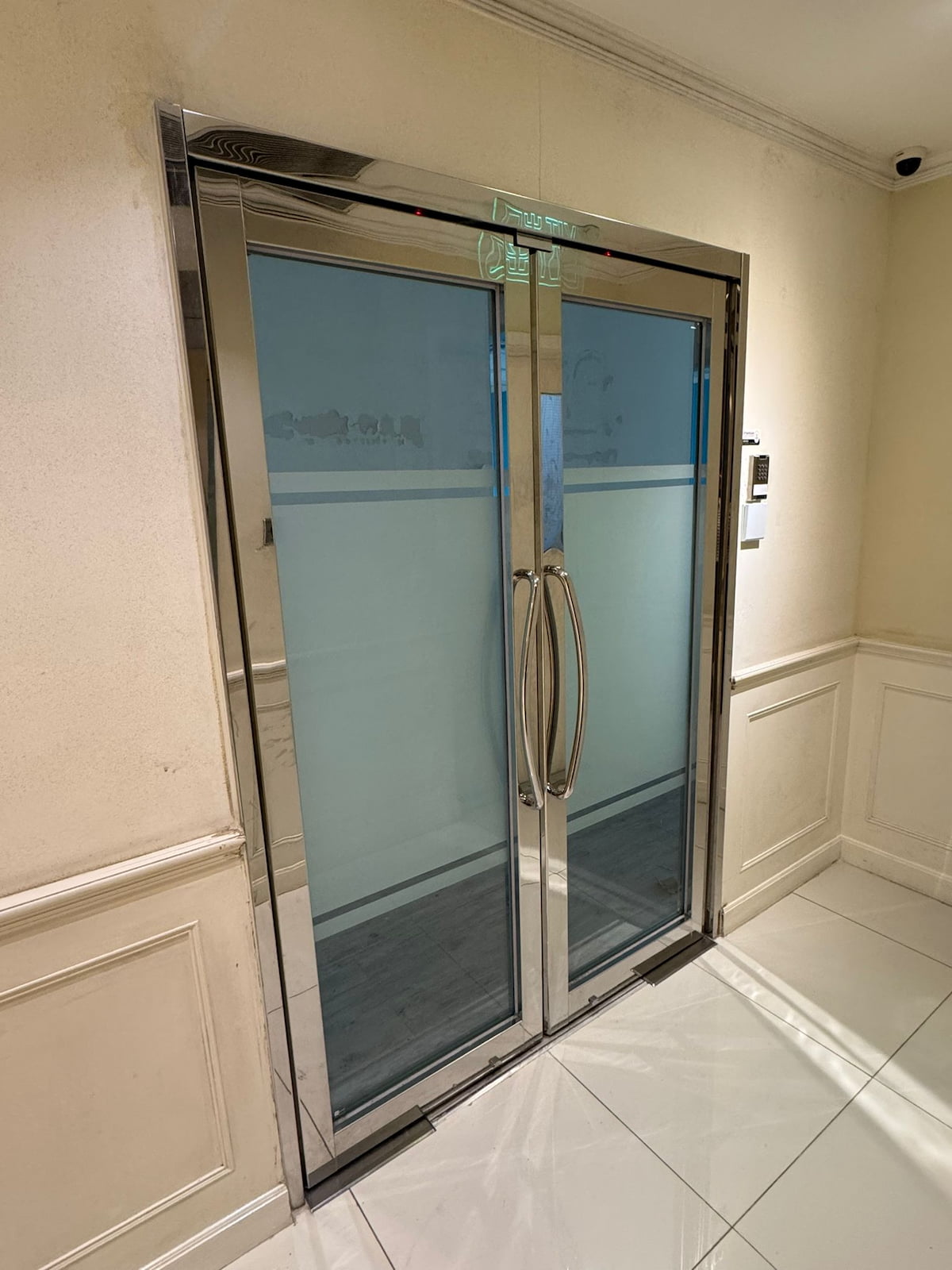 Double glass doors with metal frames in a hallway near Leighton Road, with cream walls and white tile floors.