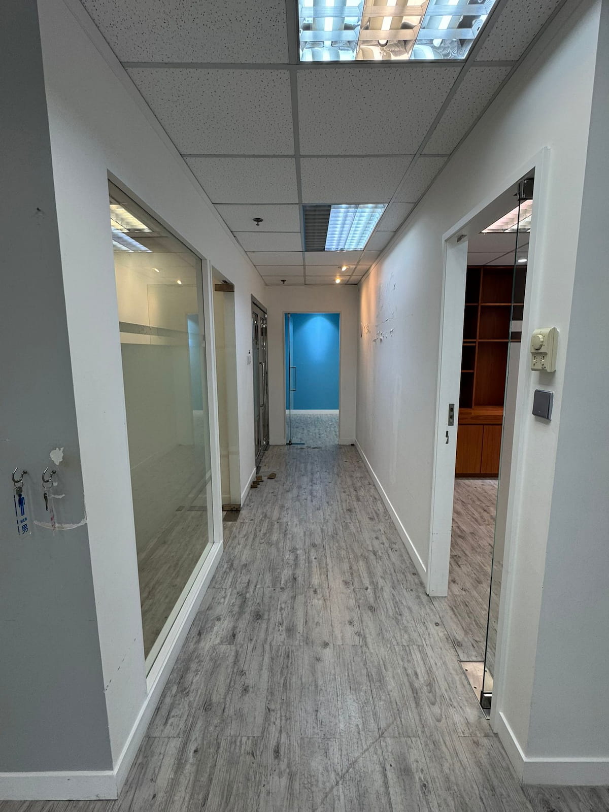 Hallway on Leighton Road with gray wood flooring, white walls, glass office doors, and a blue accent wall at the end.