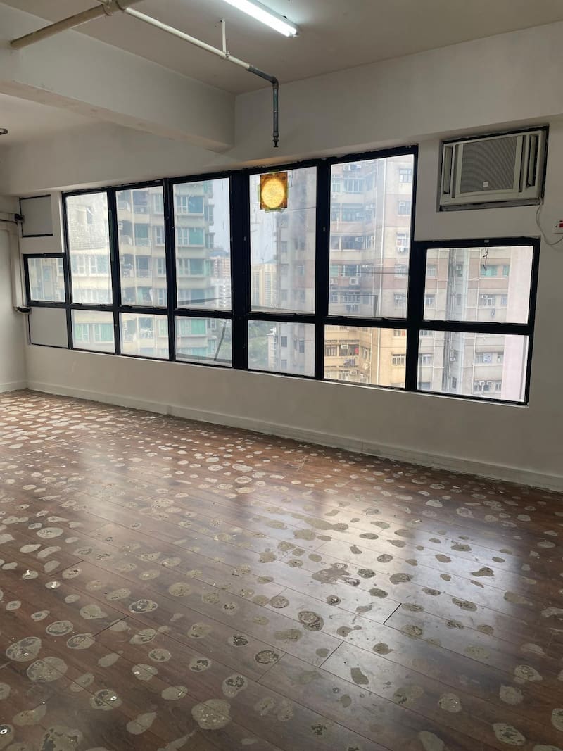 Office on Yin Chong Street, Mong Kok. Empty room with large windows, patterned wood floor, air conditioner, and view of Mong Kok Yin Chong Street apartments.