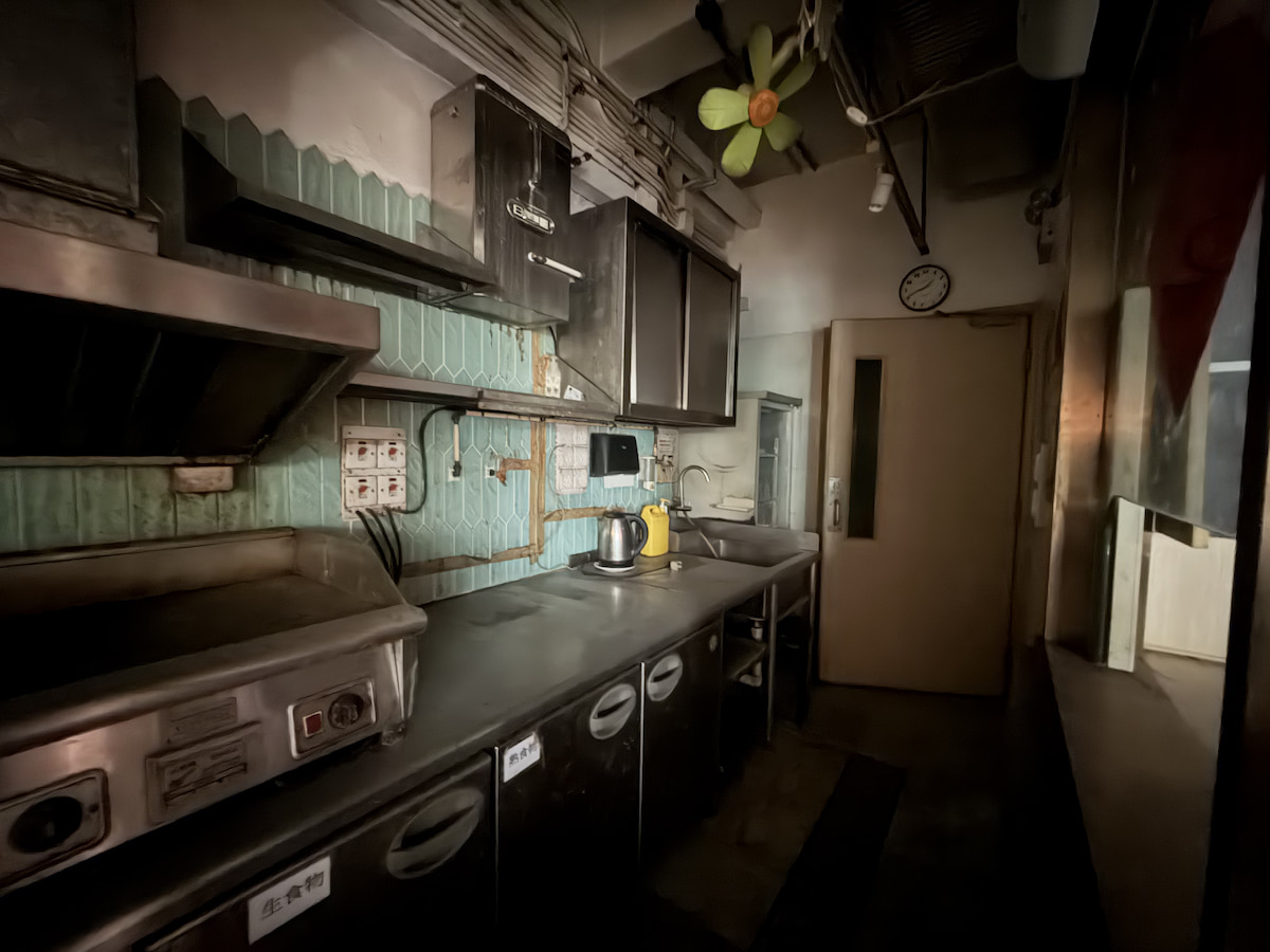 Dimly lit commercial kitchen on Lan Fong Road in Causeway Bay with metal counters, cabinets, appliances, and wall clock.