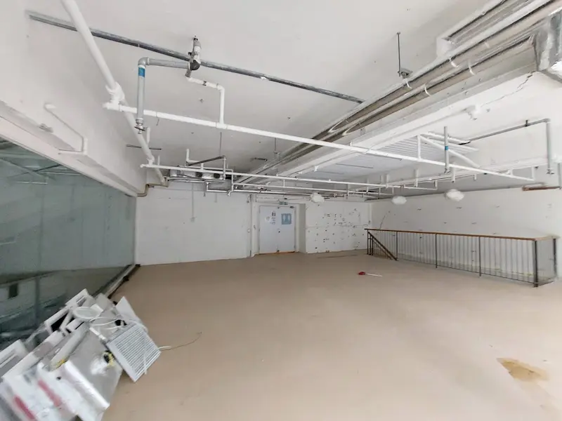 Unfinished room on Leighton Road with exposed pipes, glass wall, and debris piled near a metal railing.