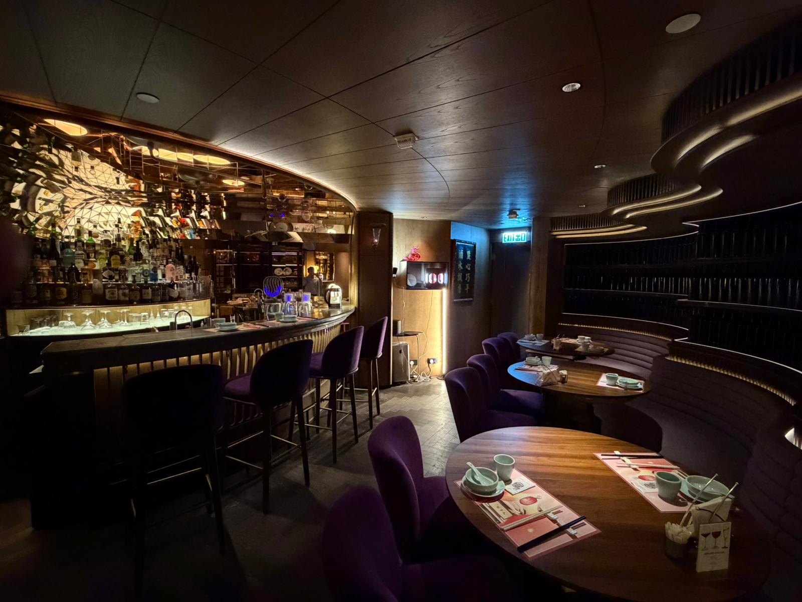 Dimly lit bar on Queen’s Road Central with a curved wooden ceiling, purple chairs, round tables, and stocked bar shelves.