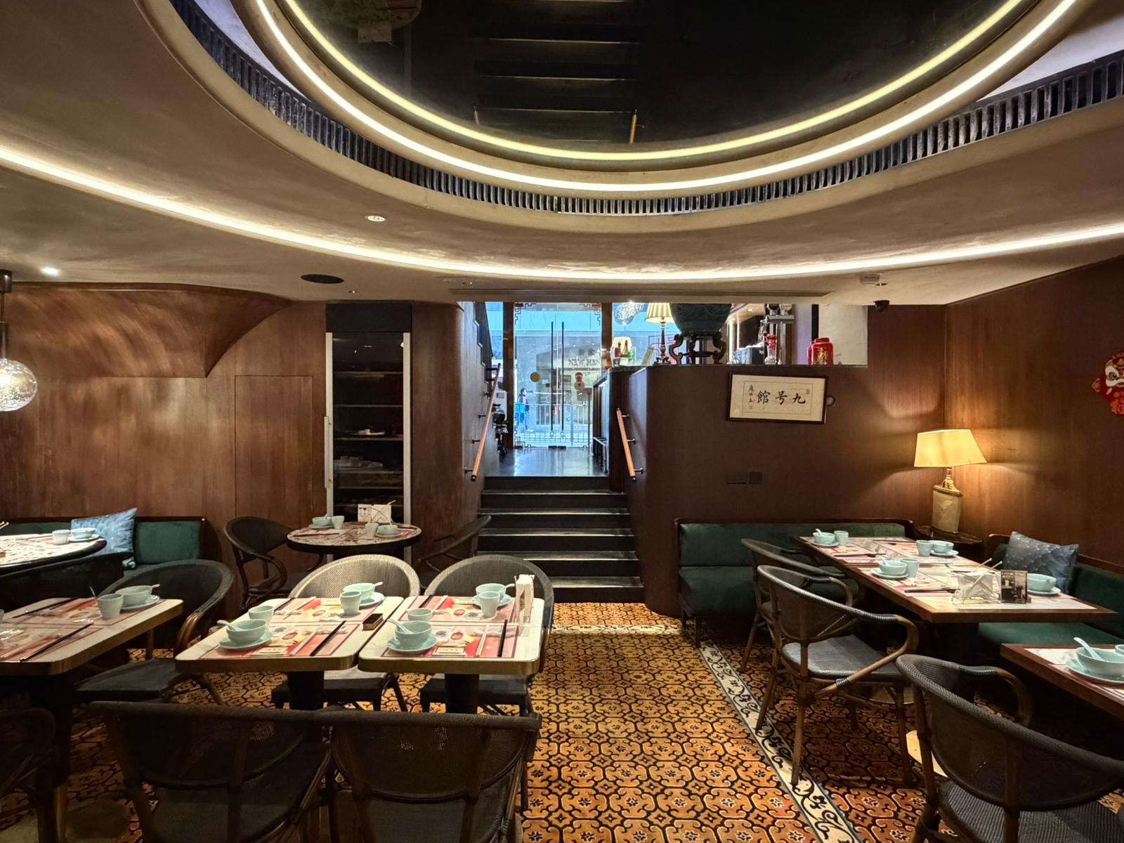 A restaurant in Central with set tables, wooden walls, a patterned floor, and a staircase leading to an upper level.