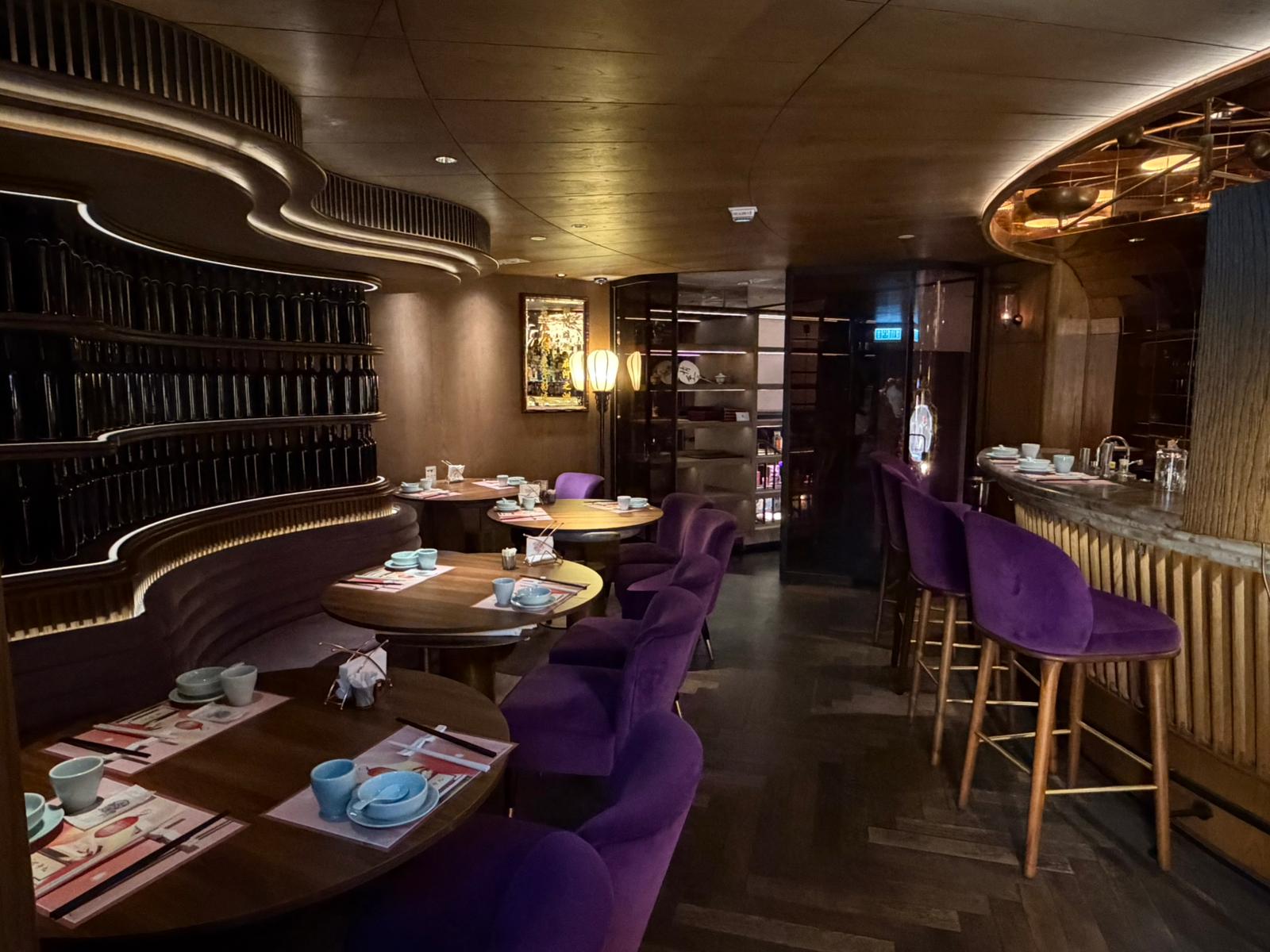 Restaurant on Queen’s Road Central with purple chairs, set tables, wooden accents, and curved shelving in low lighting.