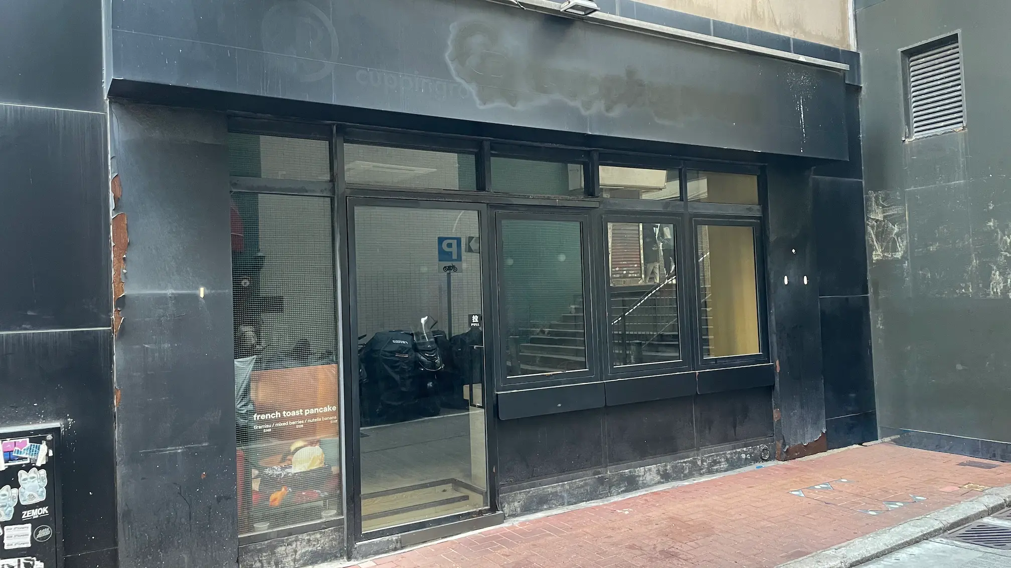Restaurant space on Queen's Road Central, Sheung Wan. Black storefront on Queen’s Road Central with glass windows, a door, empty interior, and a poster inside.