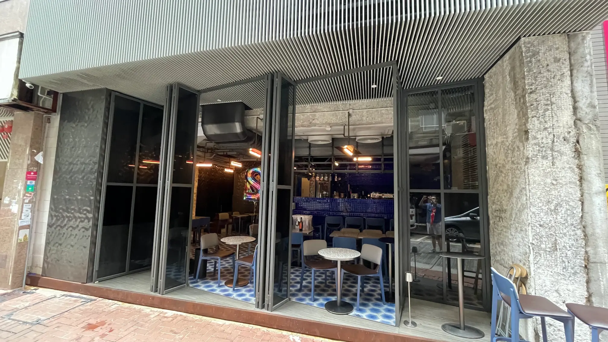 Glass-fronted cafe with round tables, blue-tiled floor, and modern decor overlooking Mercer Street in Sheung Wan.