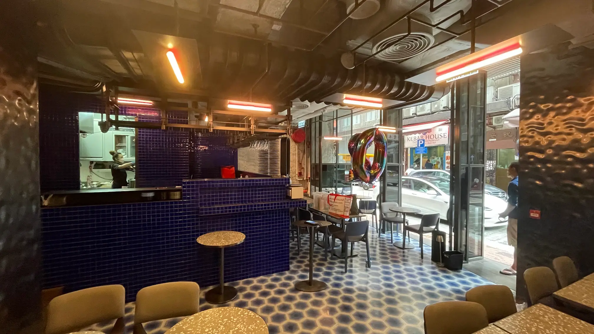 Cafe interior featuring blue tile decor, round tables, and large windows with a view of Mercer Street in Sheung Wan.