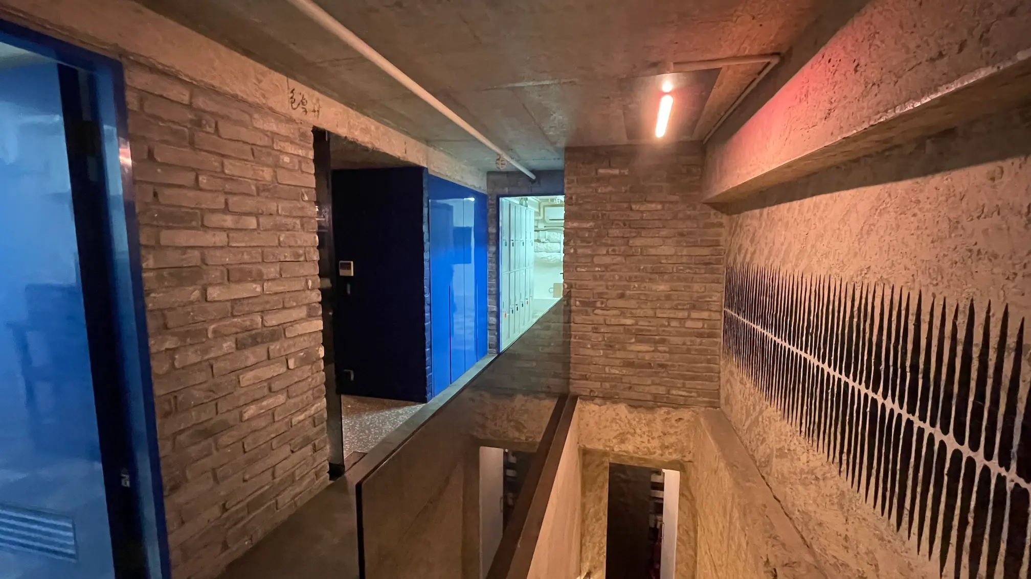 Hallway on Mercer Street, Sheung Wan, featuring brick walls, blue doors, glass railing and a ceiling light.