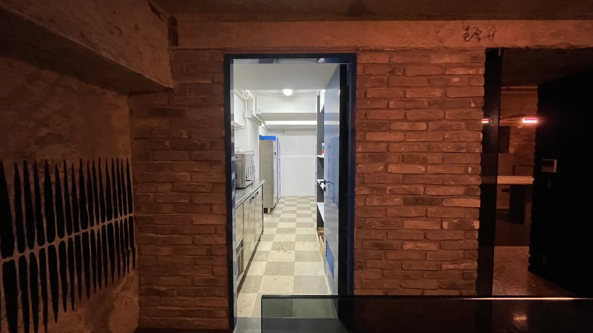A doorway in a brick wall on Mercer Street leads to a bright kitchen with checkered flooring and visible appliances.