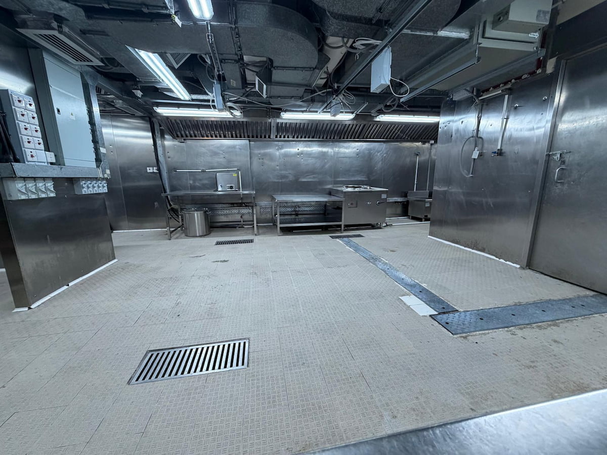 Stainless steel industrial kitchen on Wellington Street Central with metal counters appliances vents and floor drain grates.