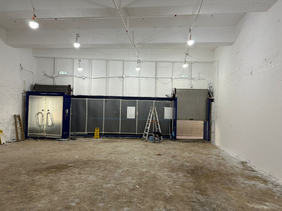 Empty warehouse on Connaught Road Central with concrete floor ladders shutters glass doors and bright ceiling lights.