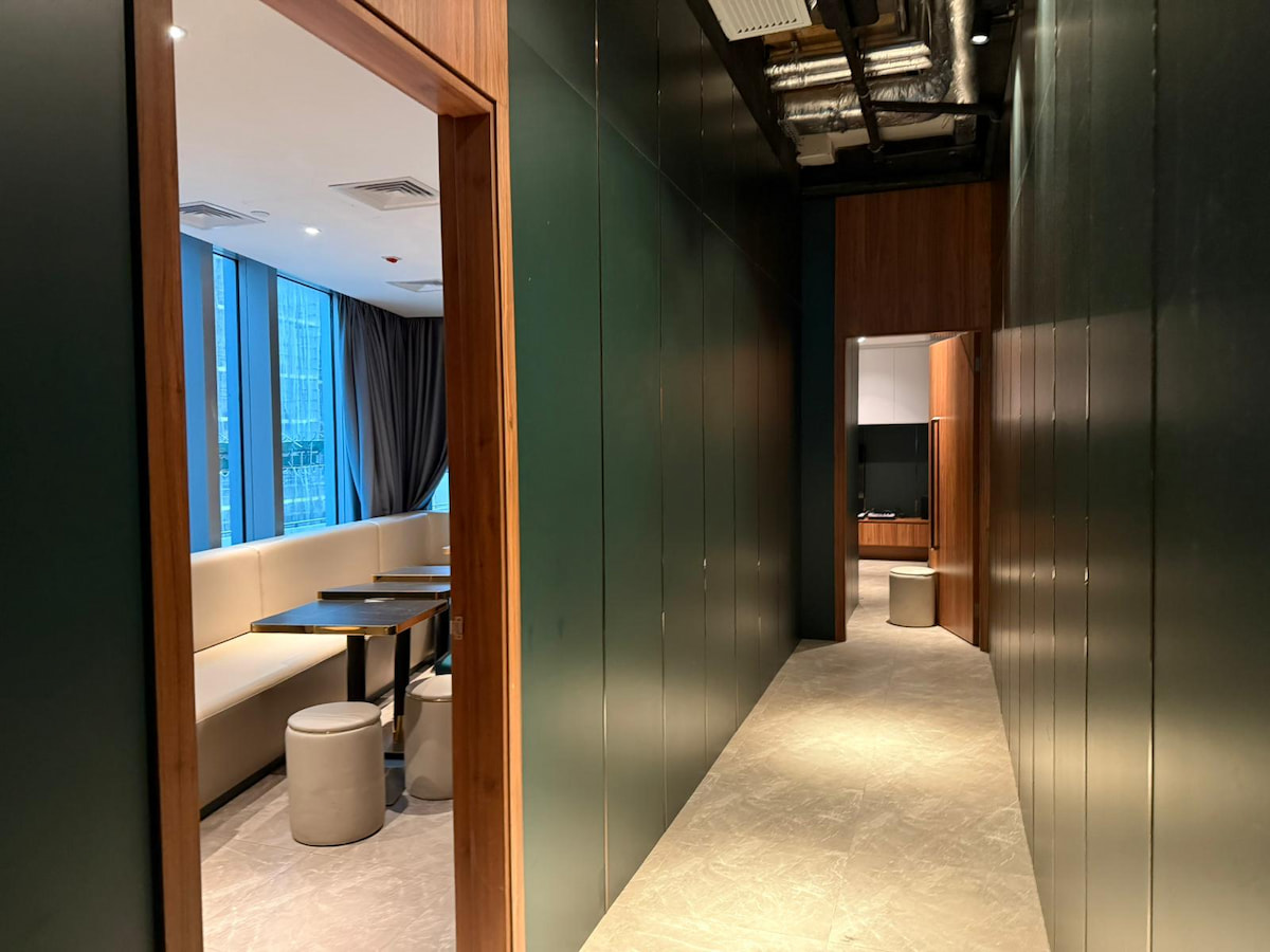A hallway with dark walls in Wong Chuk Hang leads to rooms featuring large windows and booth seating on the left.