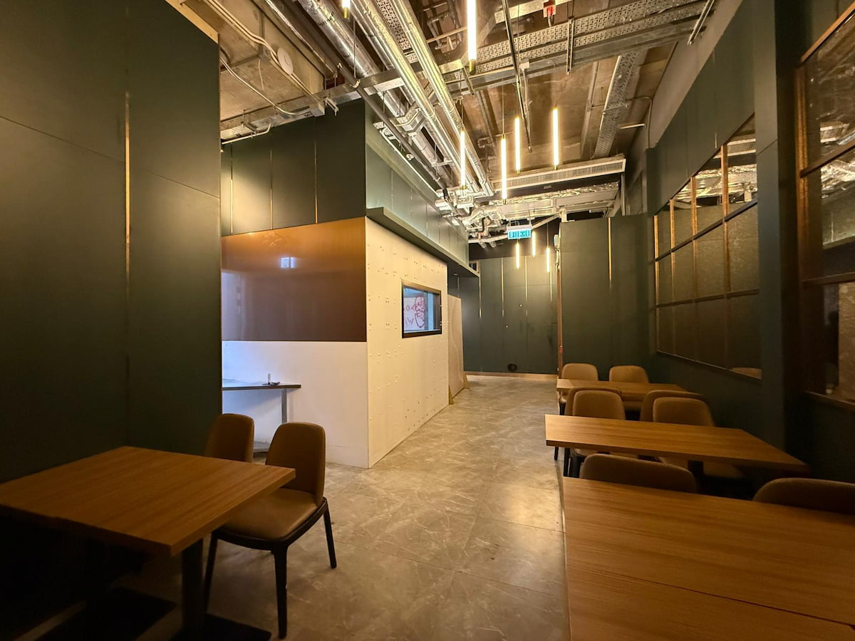 Room in Wong Chuk Hang with wood tables, exposed ceiling pipes, dark walls, and a TV mounted on a white partition.