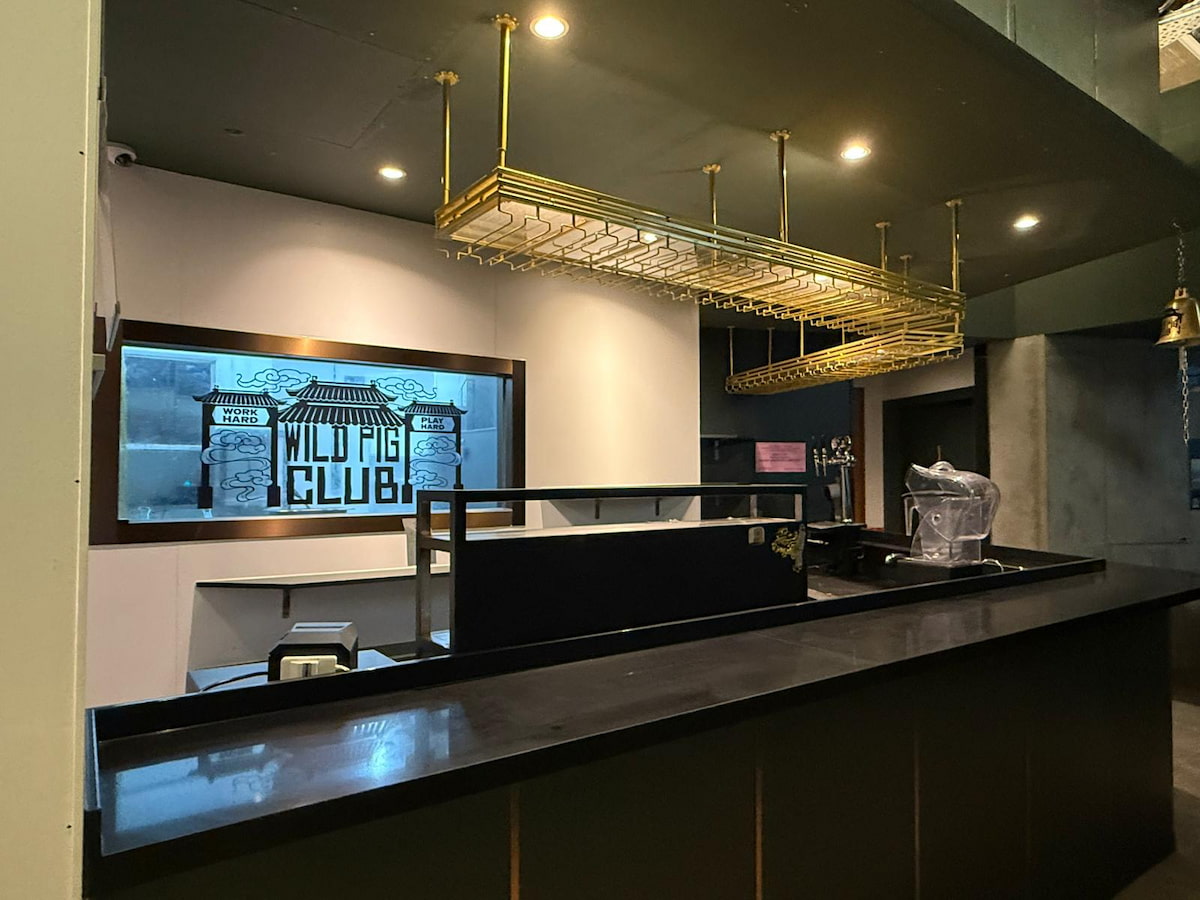 Bar on Yip Kan Street featuring a black counter, gold glass racks, and a Wild Pig Club sign on the back wall.