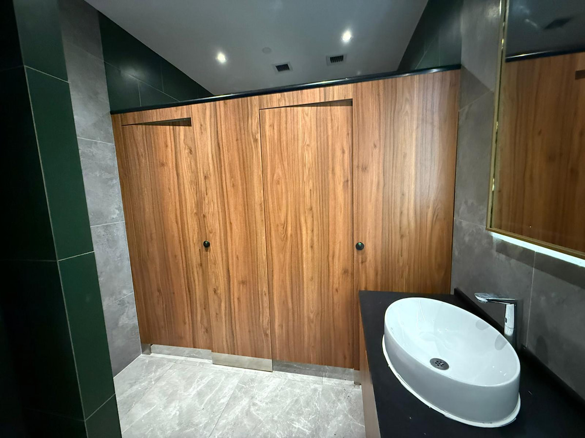 Public restroom on Yip Kan Street with wooden stall doors, a white sink, black countertop, and large wall mirror.