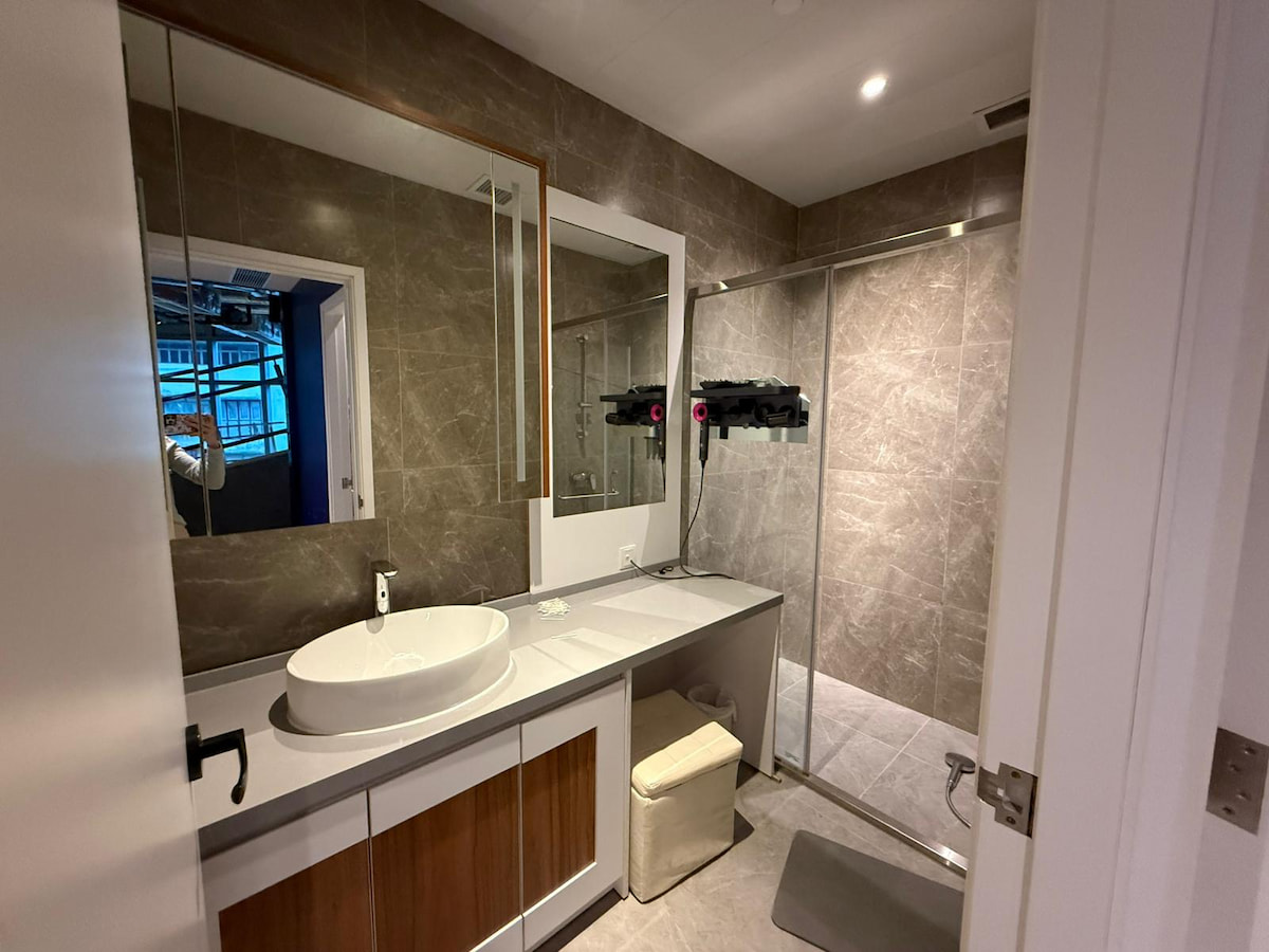 Bathroom on Yip Kan Street with gray tiles, a round sink, large wall mirror, and a glass shower enclosure.