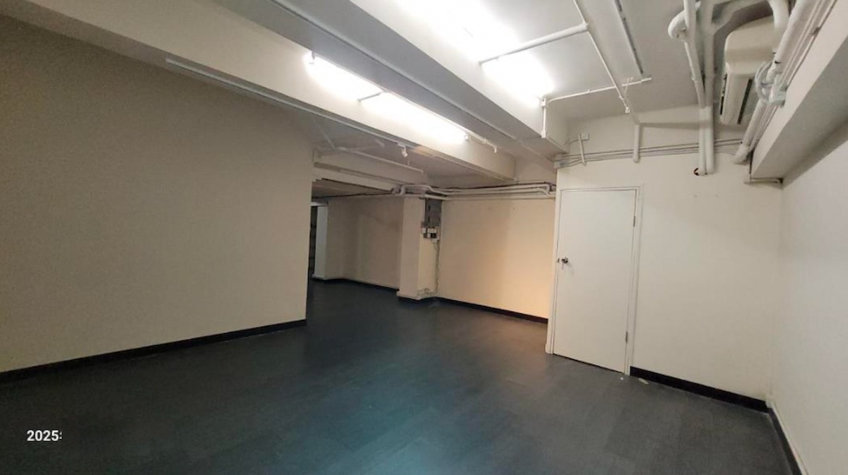 上環荷李活道一個空置房間,設有白牆、深色地板、外露天花喉管及光管照明。