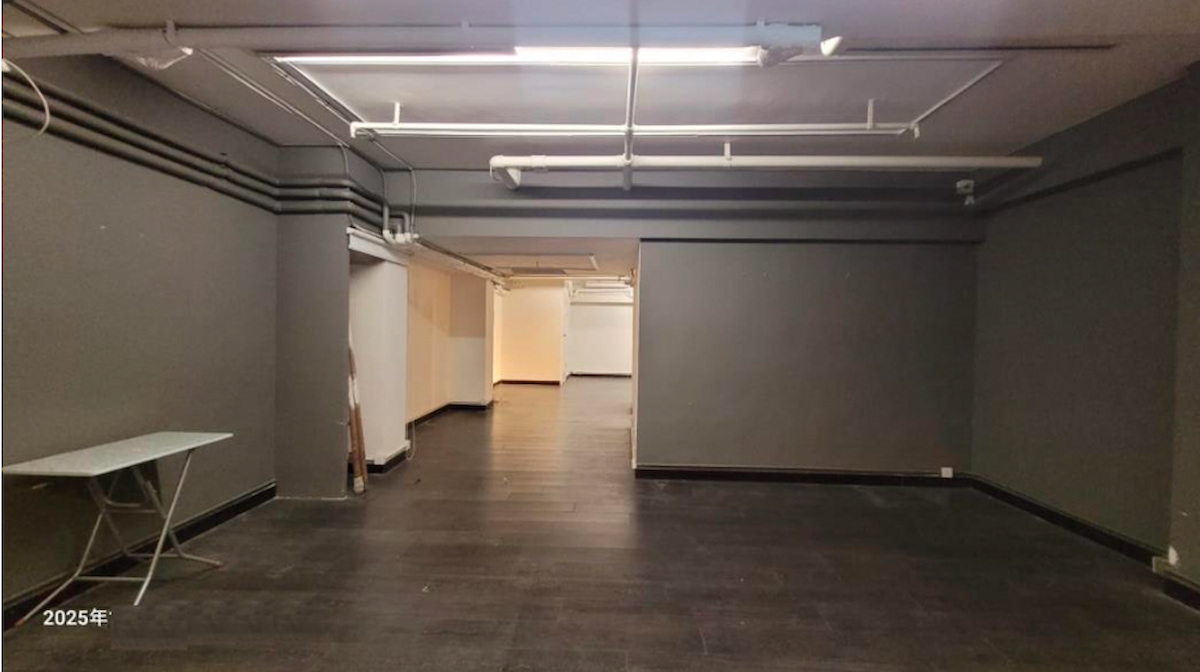 荷李活道一個空置房間,設有深色地板、灰牆、外露天花喉管,左邊有一張小枱。