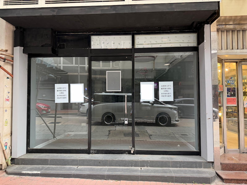 Shop on Queen's Road Central, Sheung Wan. A vacant storefront with three signs on Queen’s Road Central reflects cars and buildings from Sheung Wan across the street.