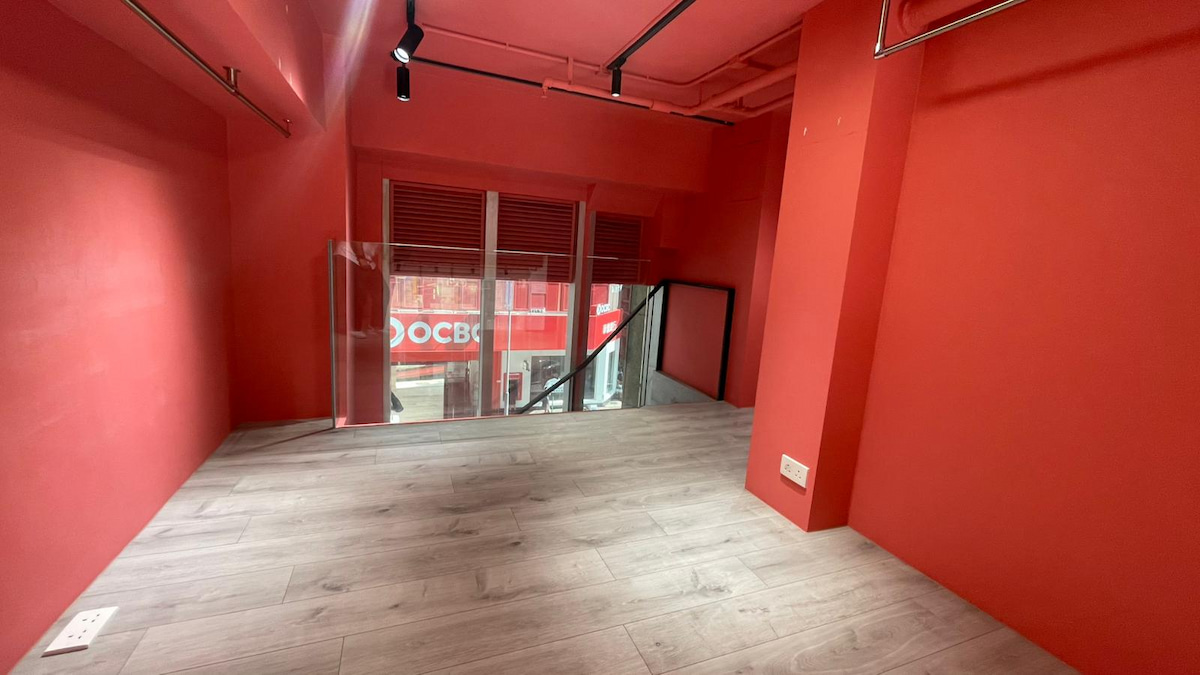 Small red room on Wellington Street with light wood flooring, glass railing, and OCBC signage visible outside in Central.
