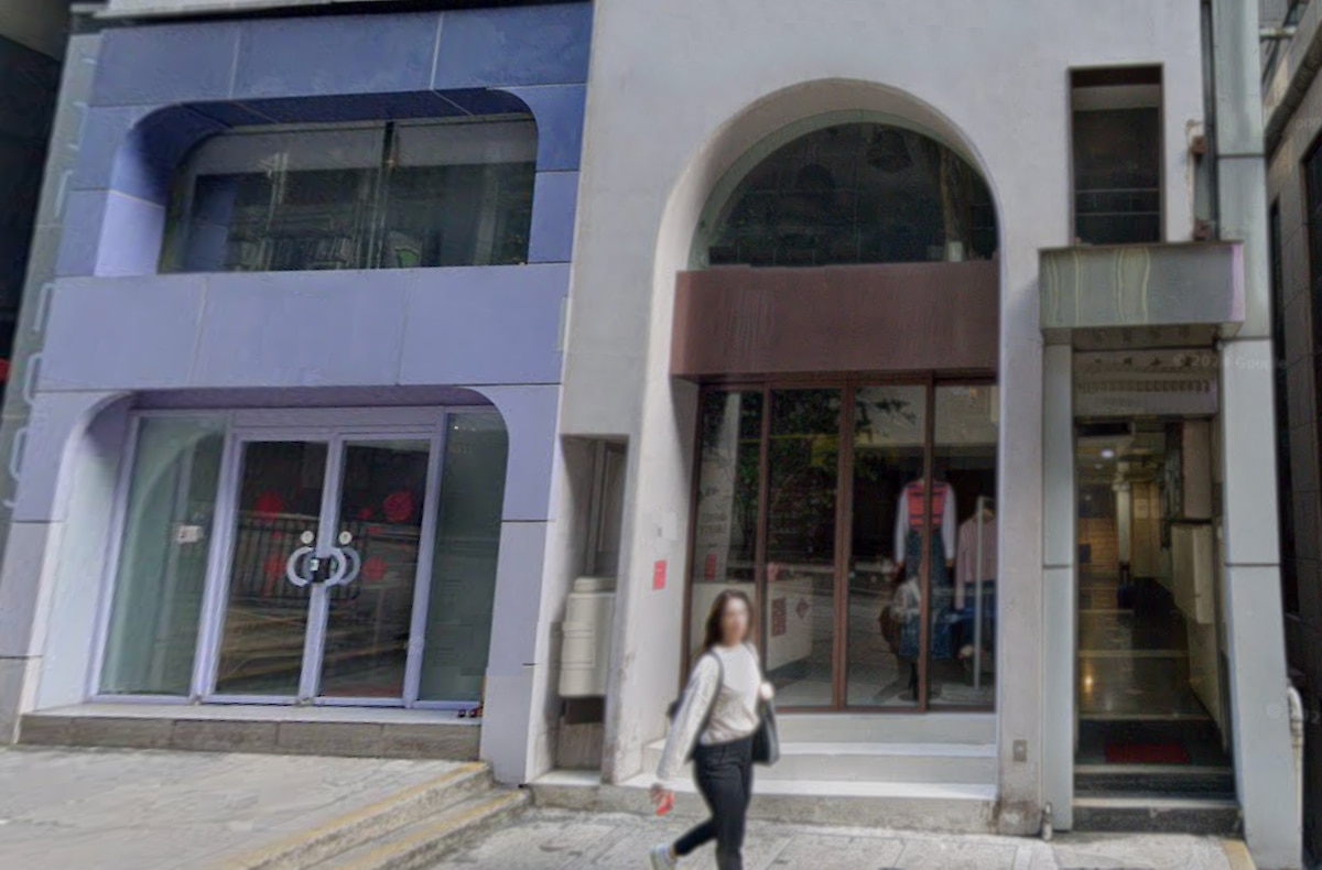 A person walks by modern buildings on Wellington Street, Central, with large arched windows and a glass entrance.