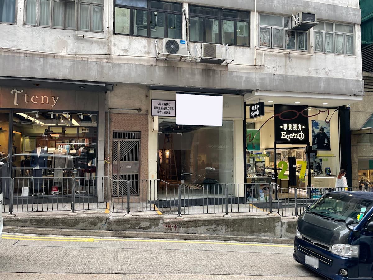 Three Central storefronts with signs and barred windows on Wellington Street, black car parked in front.