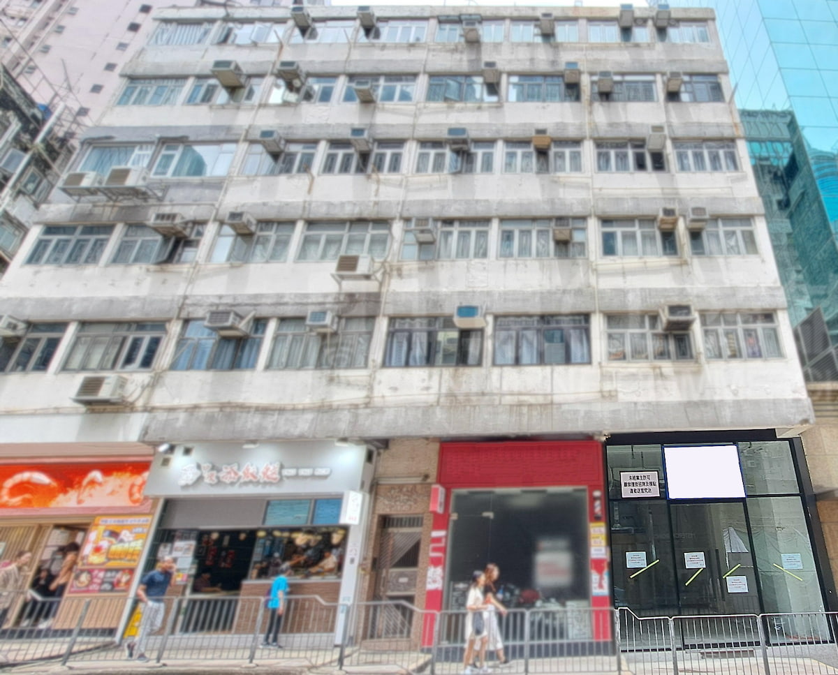A multi-story building on Wellington Street Central with shops and a restaurant on the ground floor displaying signs.