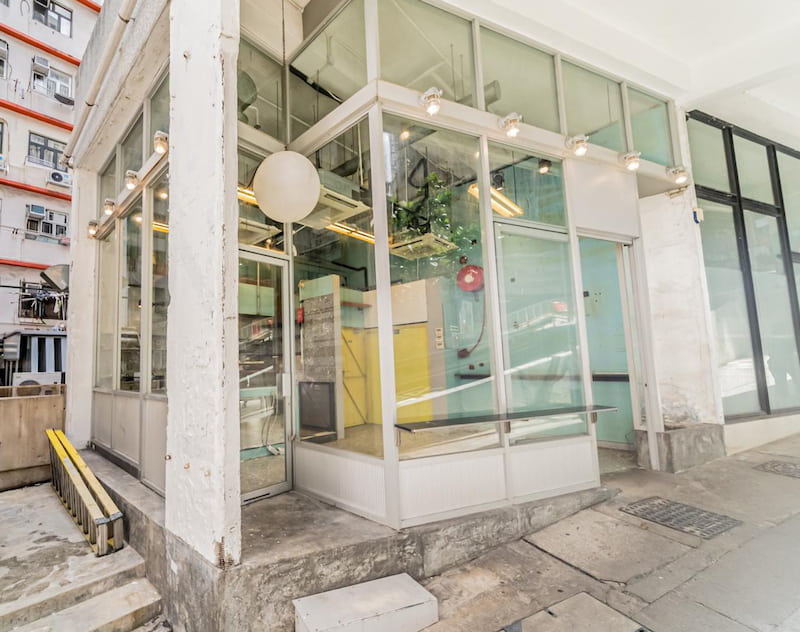 Restaurant space on Hill Road, Sai Ying Pun. Corner entrance with glass walls, featuring white walls, exposed pipes, and indoor plants.