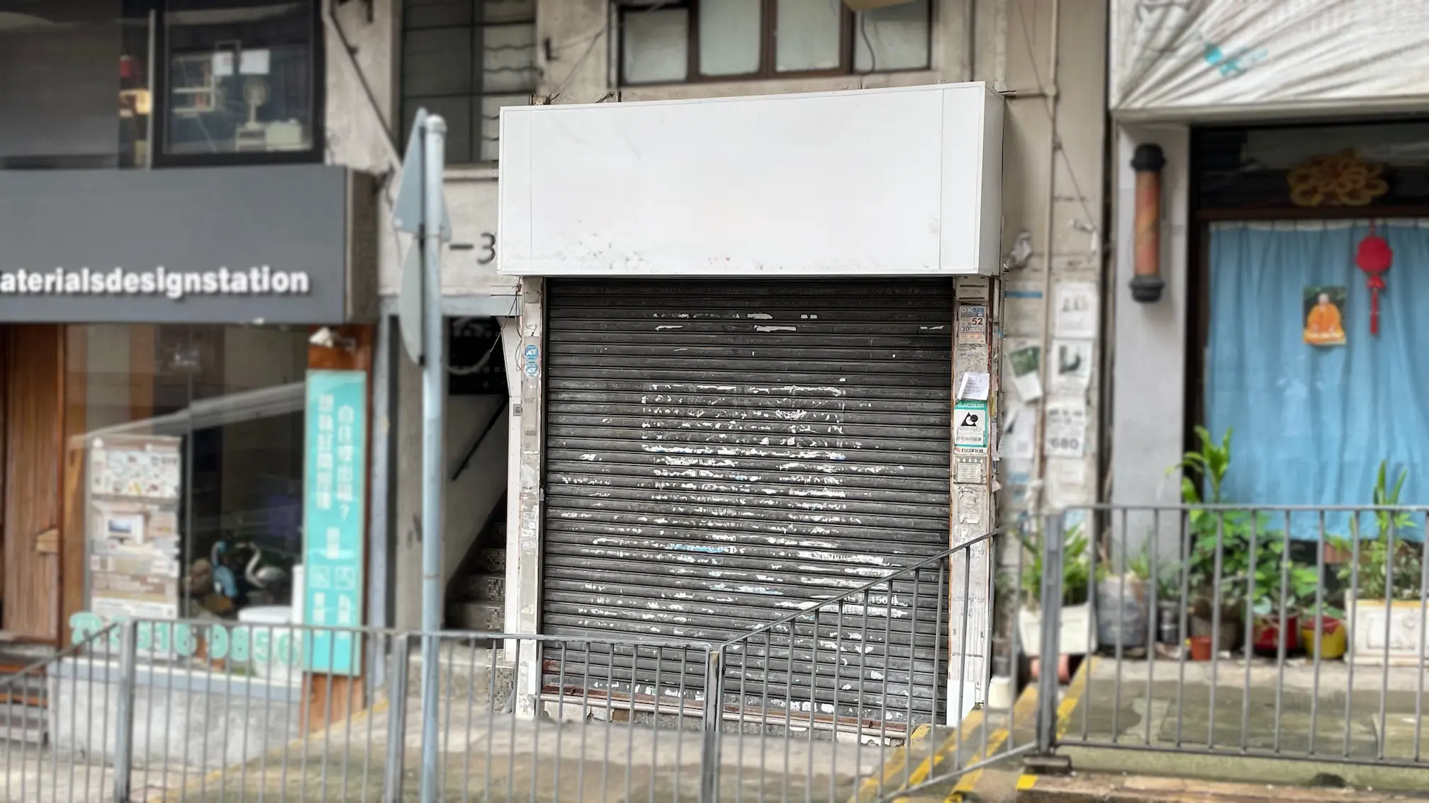 Shop on Western Street, Sai Ying Pun. A storefront has a closed metal shutter, blank sign, and a barricade on the sidewalk.