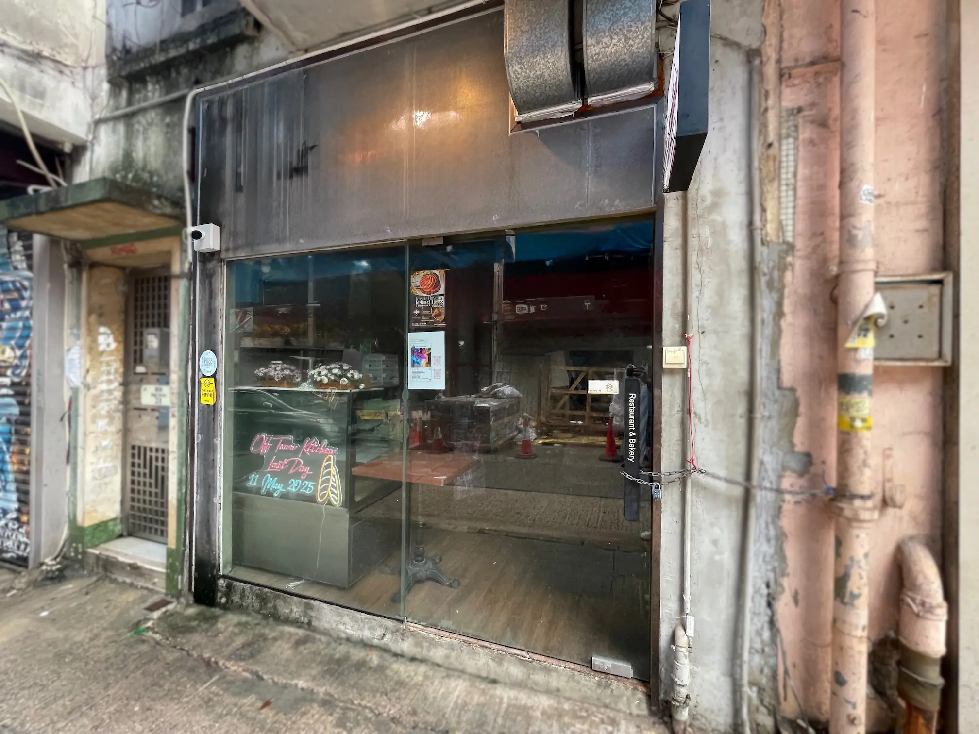 Shop on High Street, Sai Ying Pun. Glass-fronted shop with display cases and handwritten signs on a wet sidewalk.