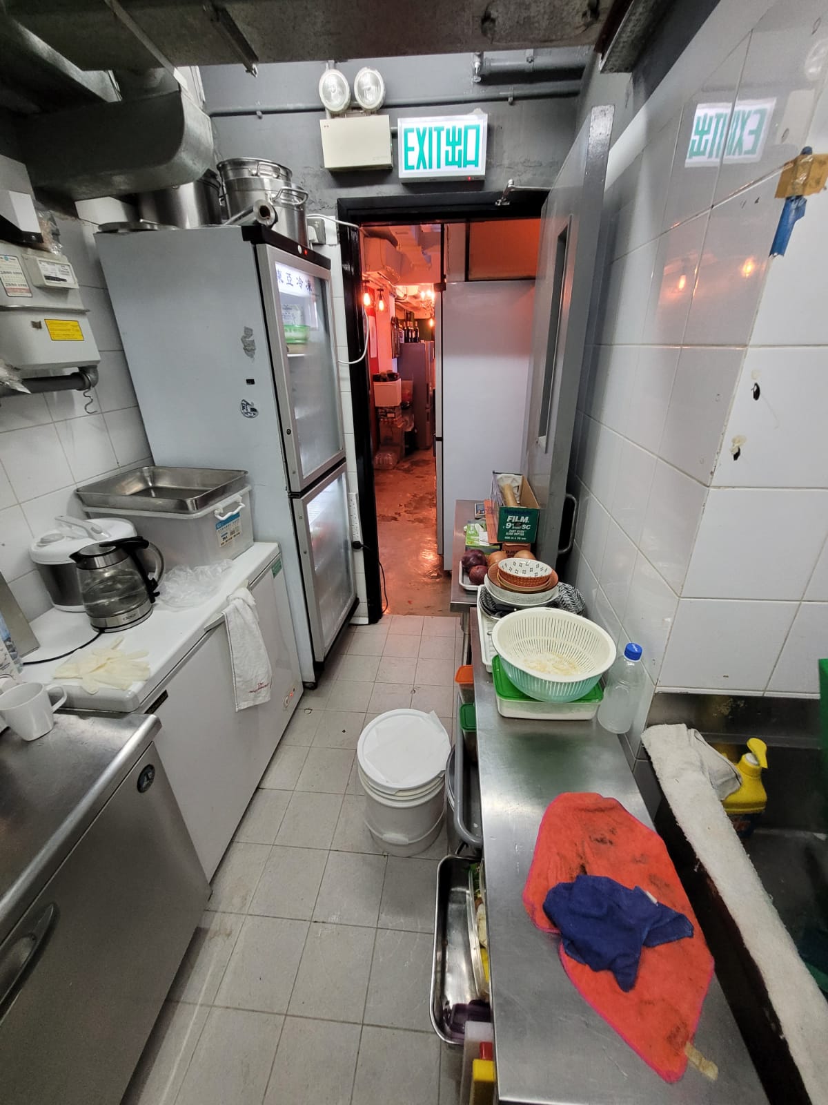 中環嘉咸街一個狹窄廚房，設有不鏽鋼電器，連接一條光線充足的走廊。