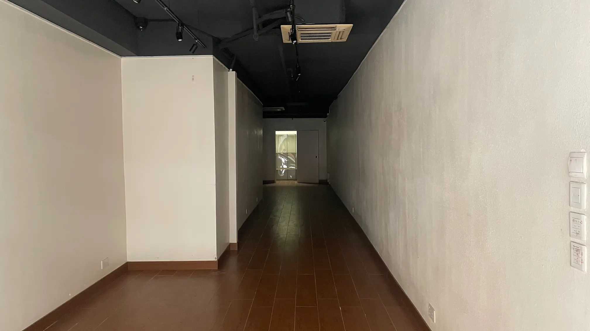 Shop on Hollywood Road, Sheung Wan. Empty, narrow room with brown tile floor and a door at the end opening to a lit area.