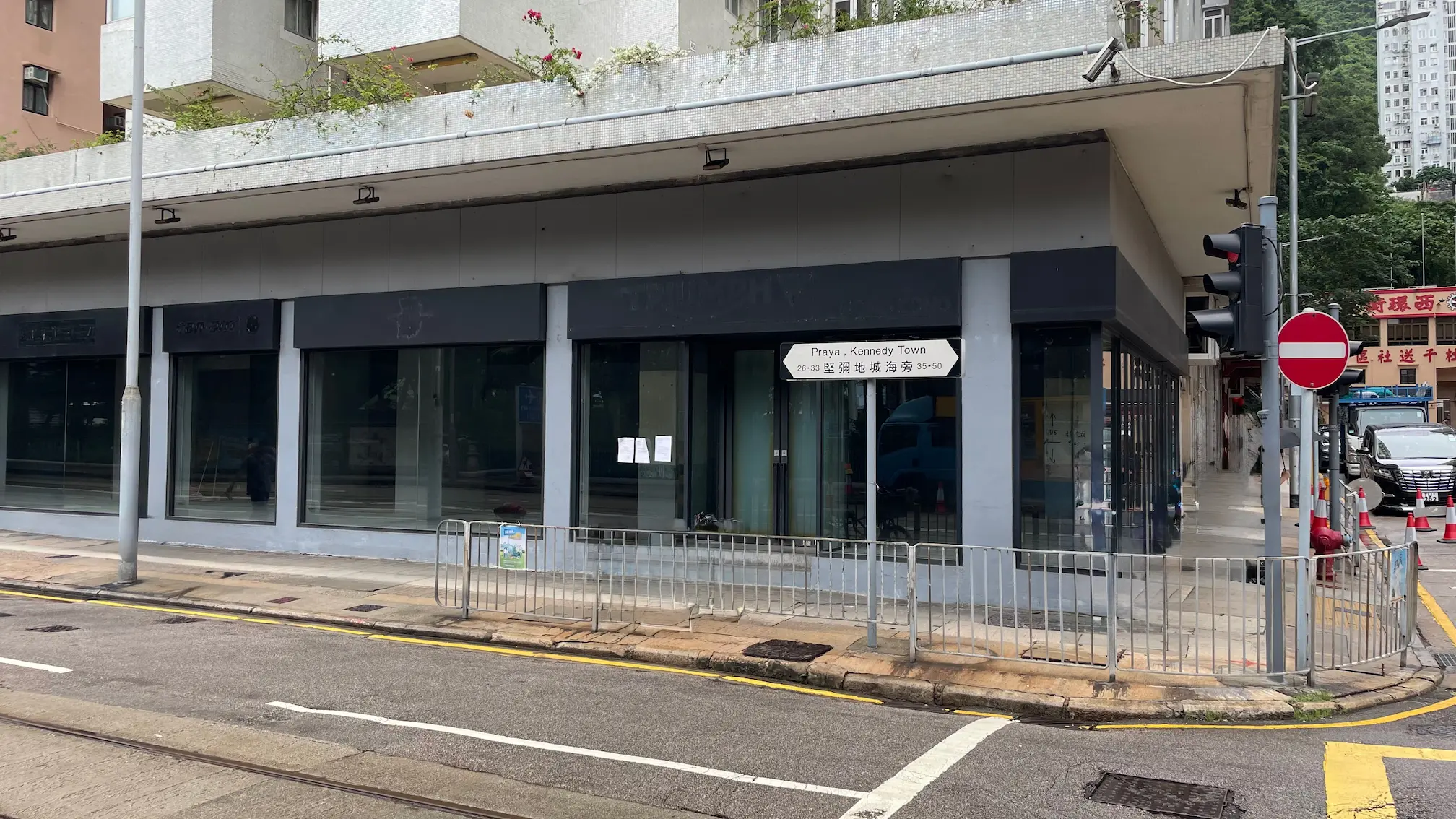 堅尼地城舖位。荷蘭街轉角一座設有大玻璃窗的灰色建築,附近設有Praya Kennedy Town街道標誌。