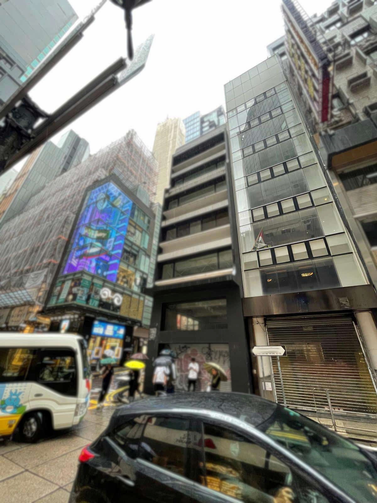 Central’s Wellington Street with tall buildings, parked cars, and people walking under umbrellas on a rainy day.