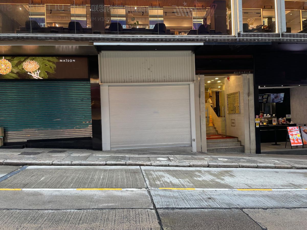 Closed storefront with metal shutter on Wellington Street, Central, located between two adjacent city businesses.