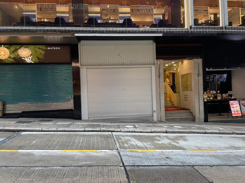 Shop on Wellington Street, Central. Closed shop with metal shutter beside another storefront and building entrance.