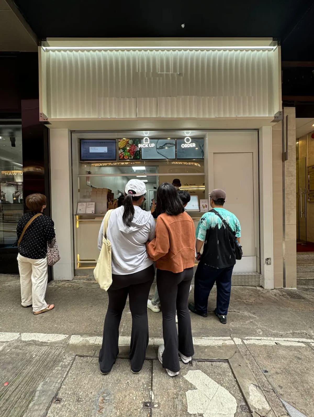 Five people stand on the sidewalk outside a storefront on Wellington Street, looking at pickup and order windows.