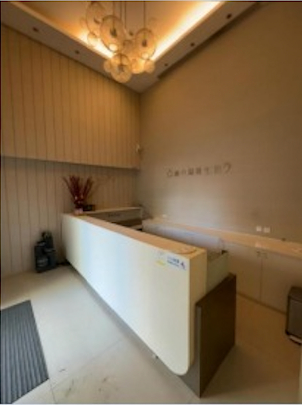Reception area on Kwong Fuk Road featuring a white desk, wall lighting, and a vase with red branches.