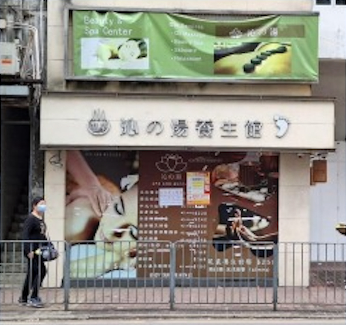 A masked person walks by a spa storefront on Kwong Fuk Road with massage signs in Chinese, English, and Japanese.