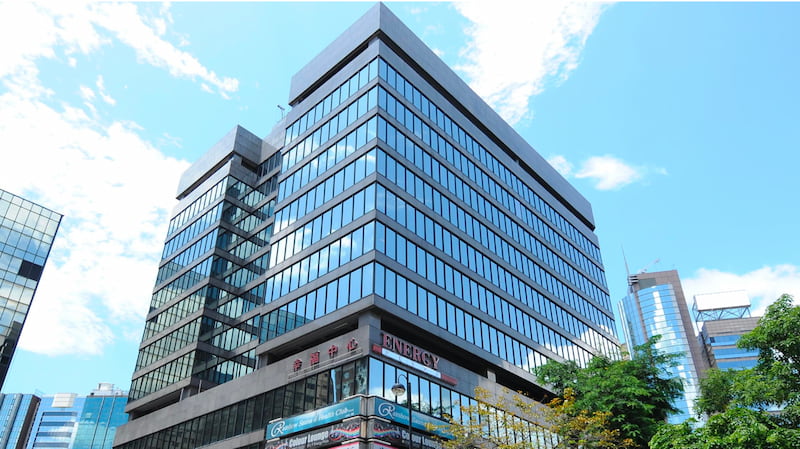 Office on Granville Road, Tsim Sha Tsui. Glass office building, surrounded by tall buildings and trees under a clear blue sky.