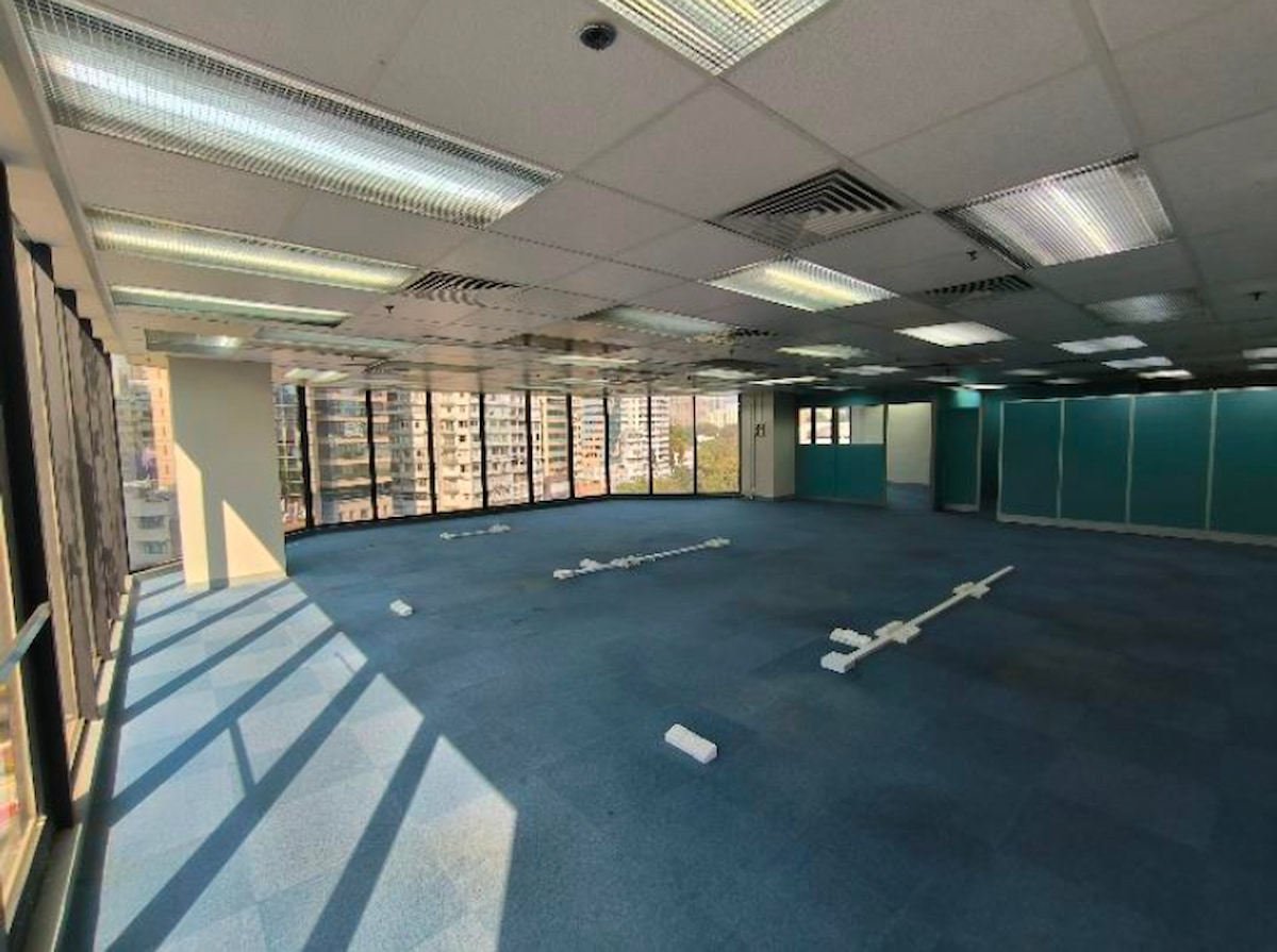 Empty Tsim Sha Tsui office with blue carpet, large windows, overhead lights, and white items scattered on the floor.