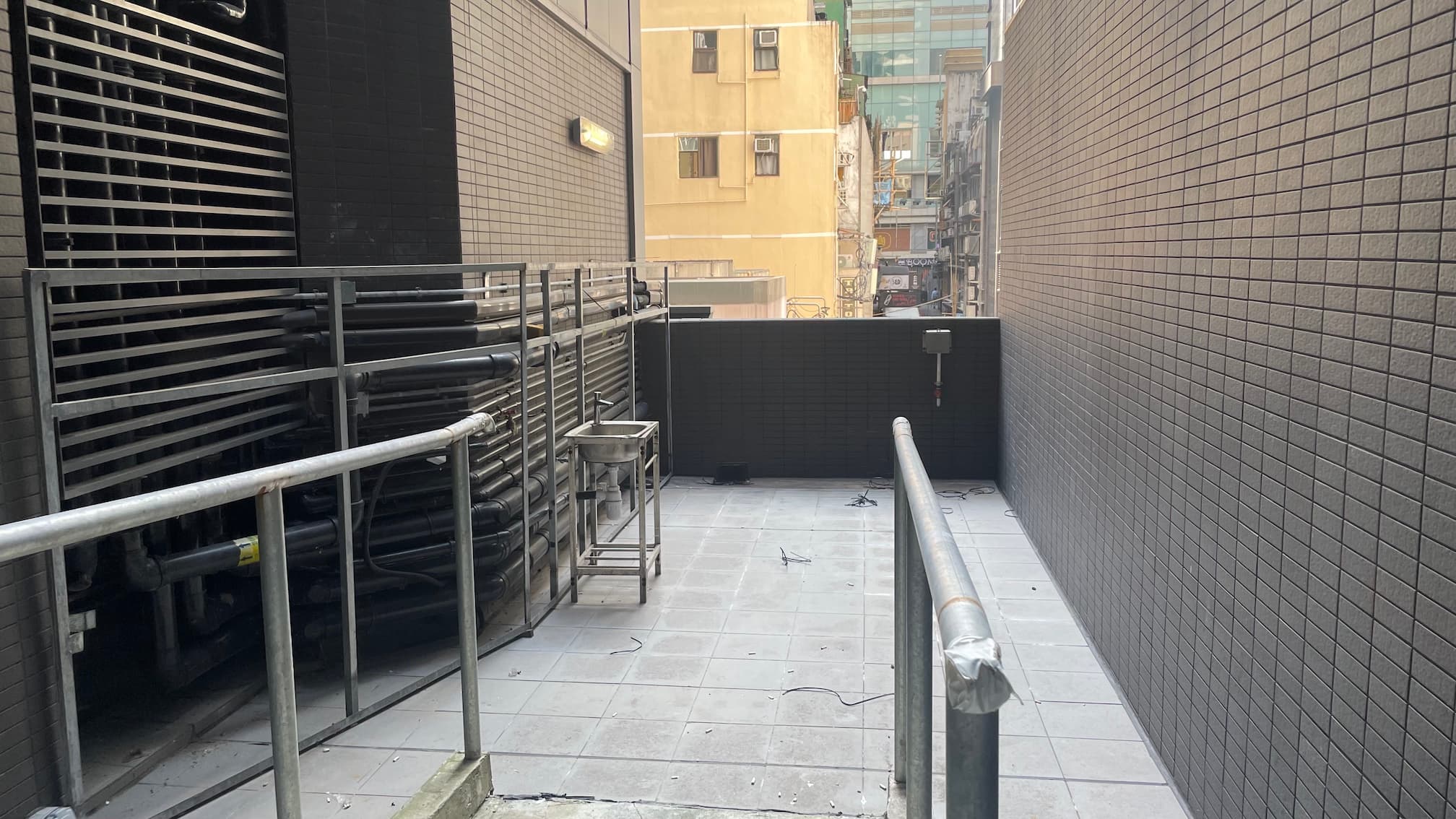 Outdoor space between buildings on Wellington Street in Central with tiled flooring, railings, and visible utility equipment.