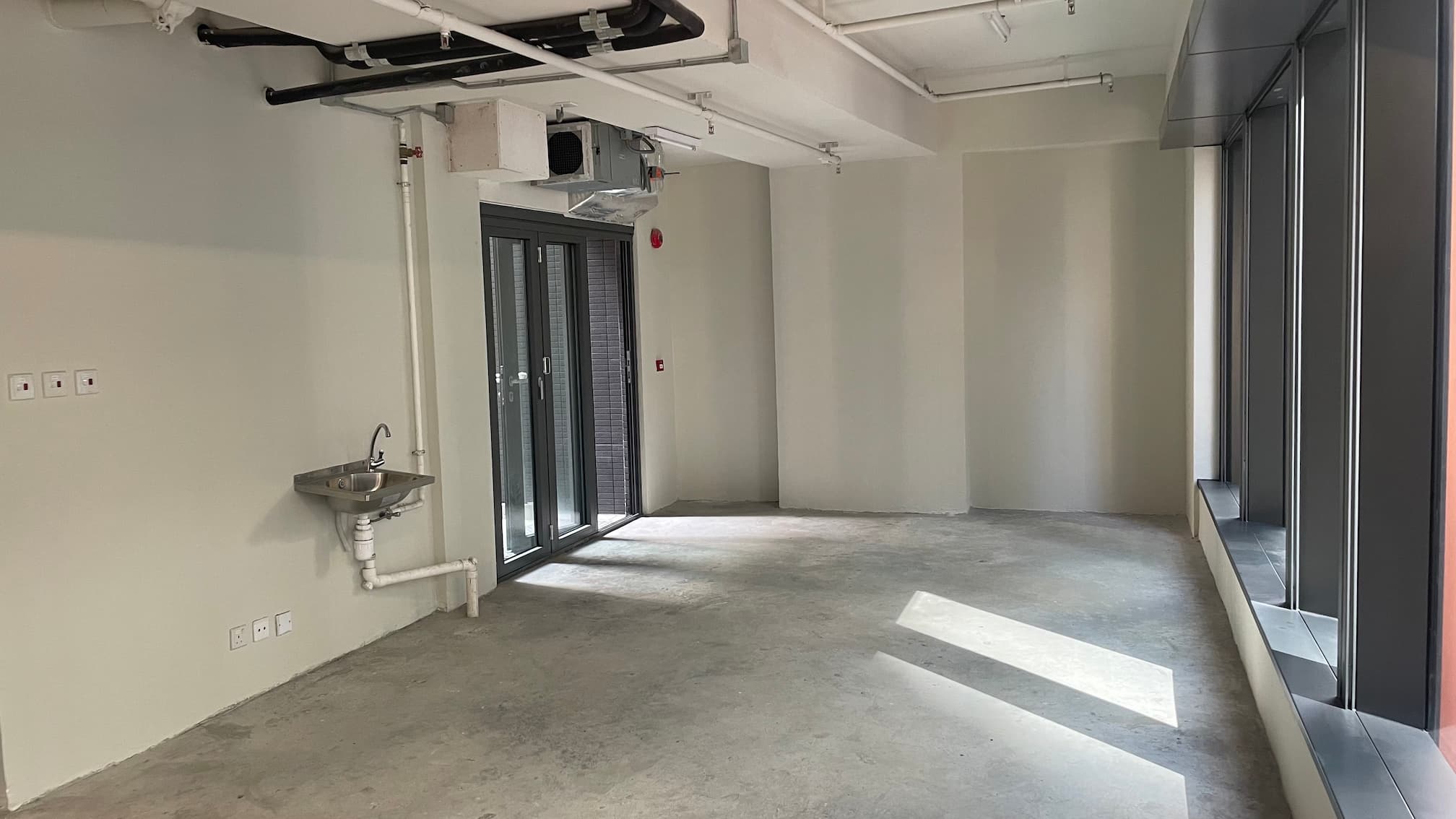 Empty room on Wellington Street featuring large windows, a concrete floor, exposed pipes, and a wall-mounted sink.
