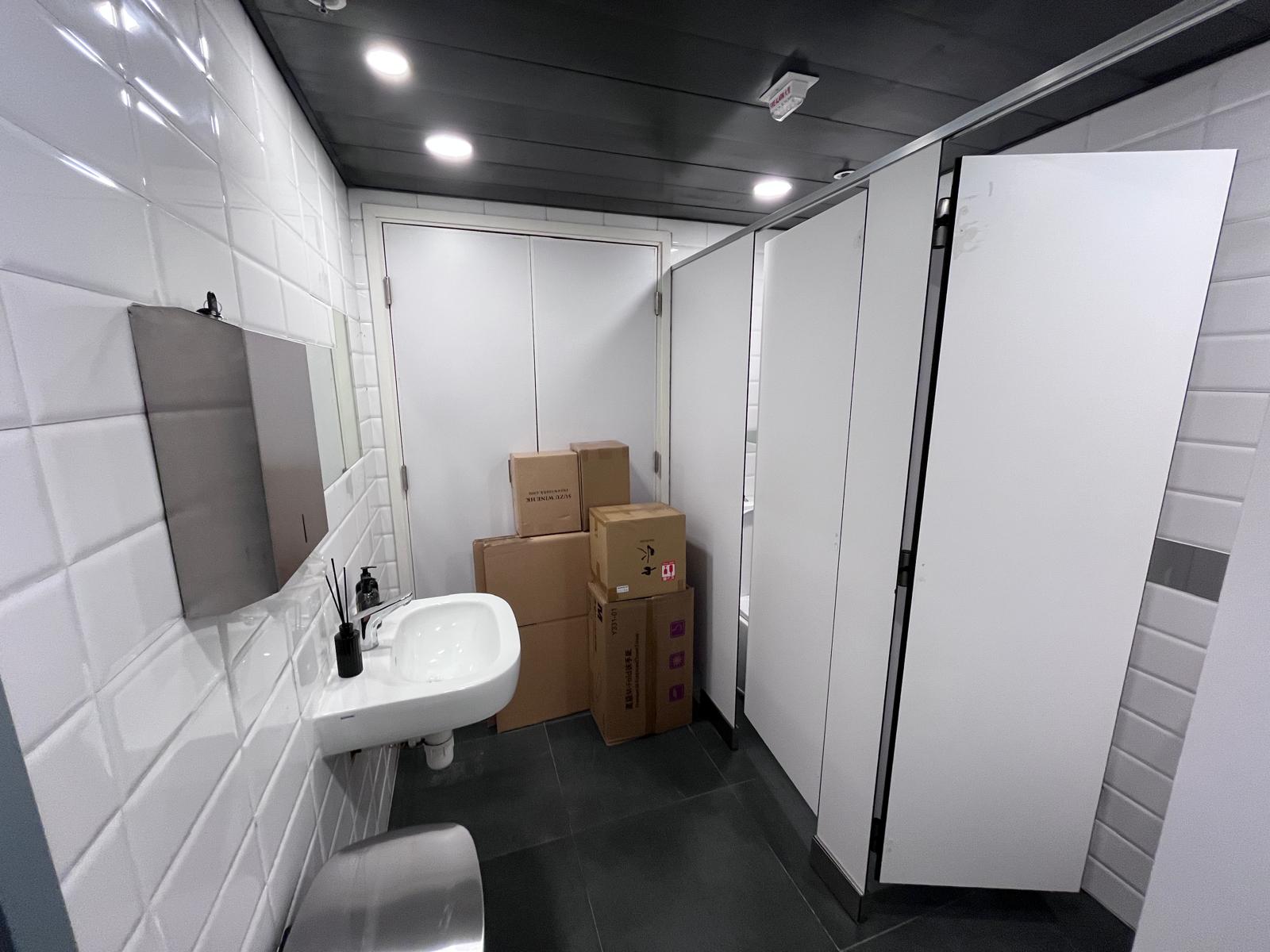 Public restroom with white tiled walls, a sink, and cardboard boxes blocking a stall on Central Wellington Street.