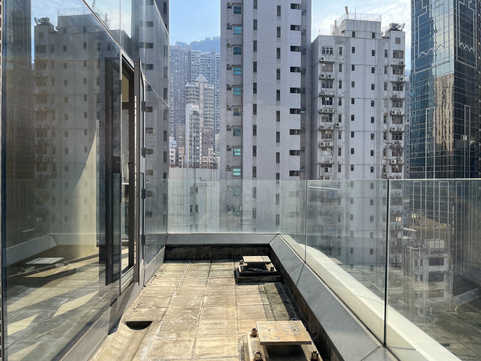 Glass balcony on a high-rise building overlooks Wellington Street and city skyscrapers in Central under a clear sky.