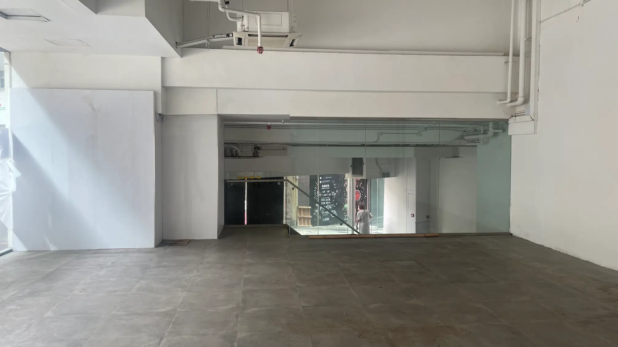 Empty commercial space with tiled floor, white walls, glass partition, and ceiling pipes on Queens Road West in Sai Ying Pun.