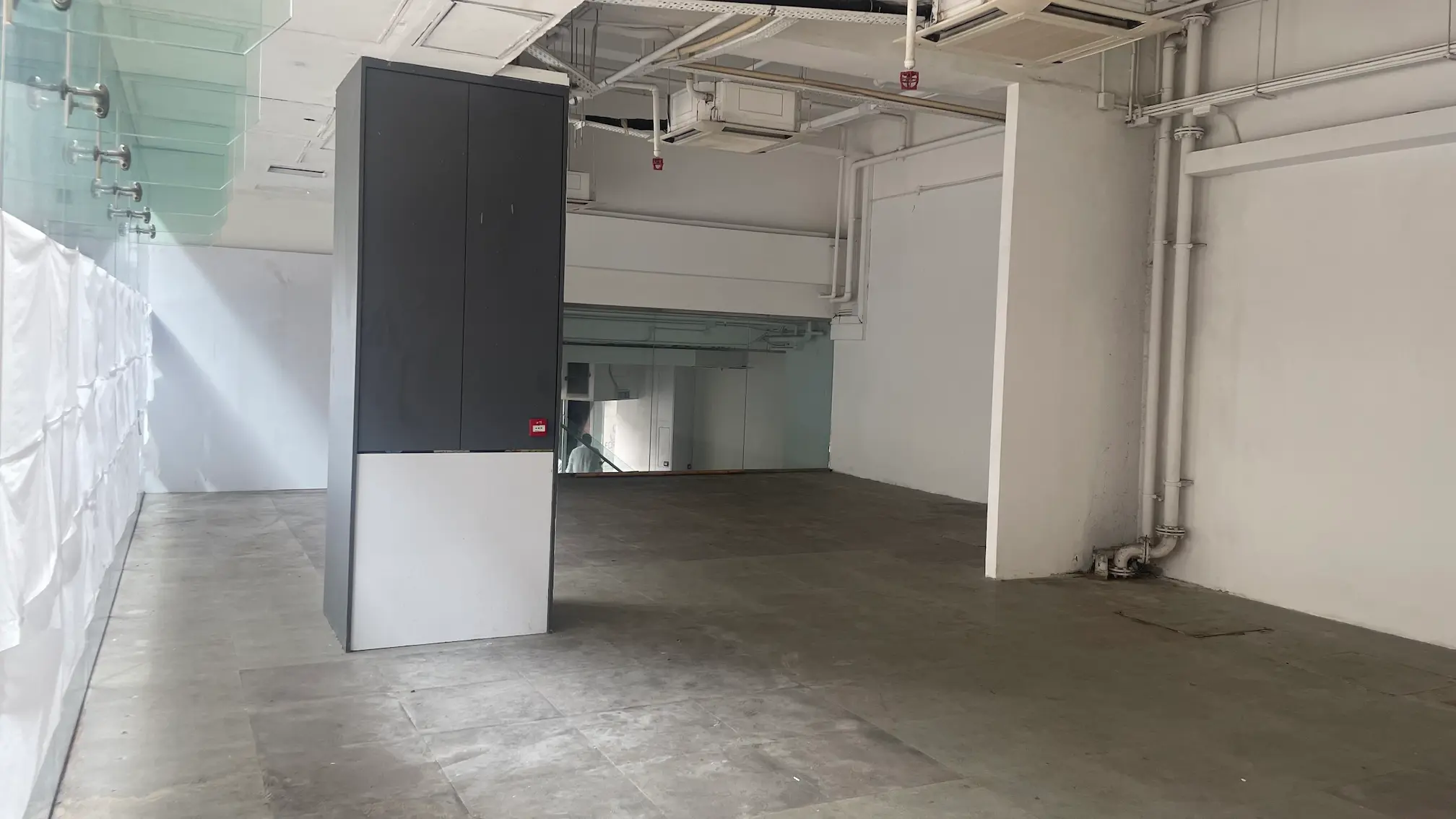 Empty commercial space on Queens Road West, Sai Ying Pun with gray floors, white walls and visible ceiling pipes.