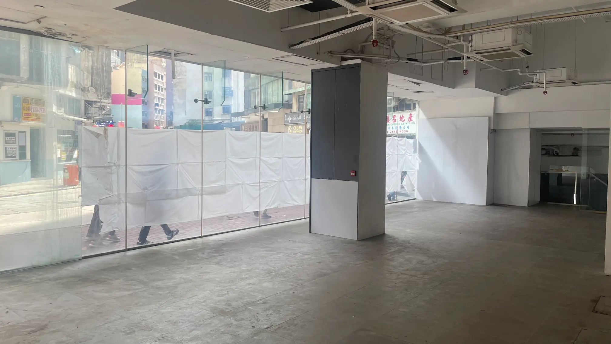 Empty interior of a storefront with large windows on Queens Road West, Sai Ying Pun; pedestrians seen outside.