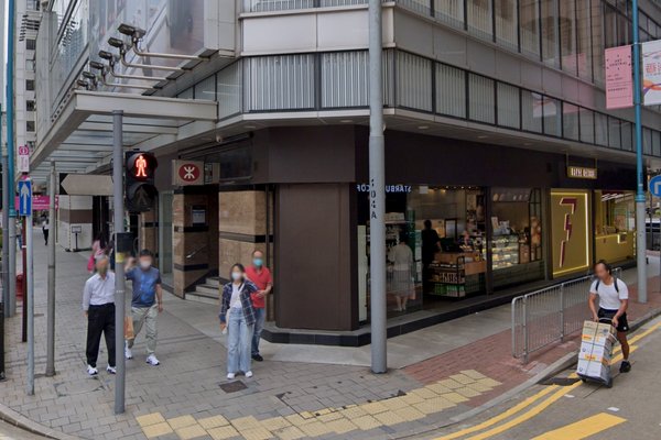 Shop on Des Voeux Road Central, Sheung Wan. Four people stand at a crosswalk with a store and entrance in Sheung Wan visible behind them.